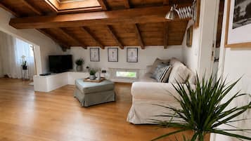 Ein großzügiges Loft mit Holzbalken, einem großen Dachfenster, einer Couch, einem Fernseher und gerahmten Bildern an den Wänden.