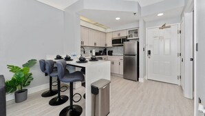 Une cuisine moderne avec des meubles blancs, un réfrigérateur en acier inoxydable et un coin bar équipé de tabourets.