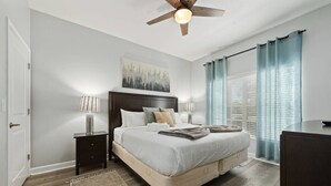 A bedroom with a bed, bedside tables, a ceiling fan, a window with curtains, and a painting on the wall. - Storey Lake Home • Pool • 15min to Disney (Kissimmee)