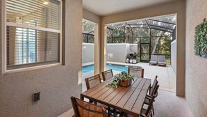 An outdoor patio with a table and chairs, a pool, and a covered area with seating. - 4BR Storey Lake Home Near Disney with Pool (Kissimmee)