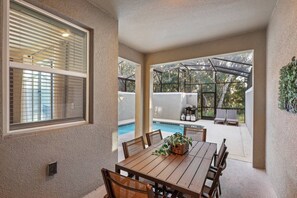 An outdoor patio with a table and chairs, a pool, and a covered area with seating. - 4BR Storey Lake Home Near Disney with Pool (Kissimmee)