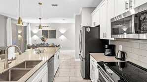 A modern kitchen with stainless steel appliances, a central island, pendant lighting, and a view into the dining area. - 4BR Storey Lake Home Near Disney with Pool (Kissimmee)