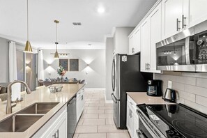 A modern kitchen with stainless steel appliances, a central island, pendant lighting, and a view into the dining area. - 4BR Storey Lake Home Near Disney with Pool (Kissimmee)