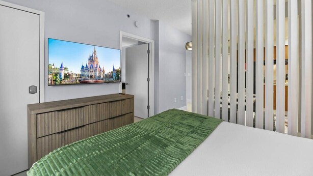 Ein Hotelzimmer mit einem Bett, einem an der Wand montierten Fernseher, einer Holzkommode und einem grünen Teppich.