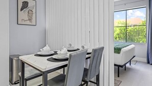 Ein moderner Essbereich mit einem Tisch für vier Personen, einem Bett mit grüner Decke und einem Fenster mit Blick auf Grünflächen.