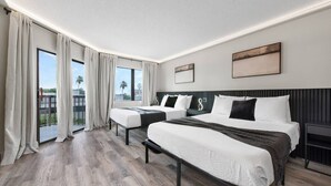 A modern hotel room with two beds, a large window with curtains, a view of palm trees, and a painting on the wall. - Modern Studio at The Enclave Near Universal (Orlando)