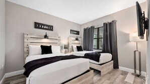 A bedroom with two beds, a window with curtains, a flat-screen TV, and a wall-mounted artwork. - 2BR Suite at The Enclave—Near Universal (Orlando)