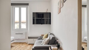 Ett modernt vardagsrum med en grå soffa, ett litet träbord, en väggmonterad TV och ett fönster med utsikt.