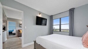 Quarto com cama, televisão na parede, janela com cortinas e vista para o exterior.