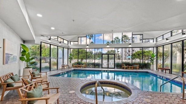 Ett modernt inomhuspoolområde med bubbelpool, solstolar och utsikt över stadsbilden.