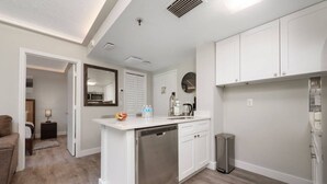 Una cucina compatta con mobili bianchi, lavastoviglie e cestino.