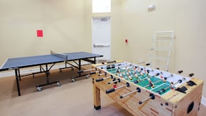 Una habitación con mesa de ping pong, mesa de fútbolín, una puerta blanca y una ventana.