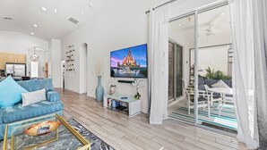 Una sala de estar moderna con un televisor de pantalla plana, un sofá azul, una mesa de centro y un ventanal que da a un área de estar exterior.