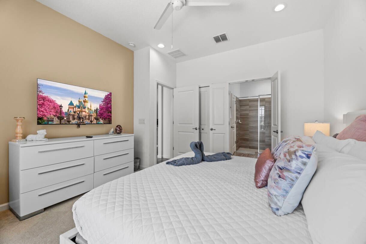 A bedroom with a bed, a dresser, a television, and a door leading to a bathroom.