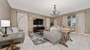 Un salon moderne avec un canapé, une table basse, un téléviseur et un lustre.