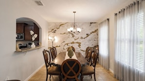 Ein Esszimmer mit Marmorwand, einer Chandelierleuchtre und einer durch einen Bogen sichtbaren Küche.