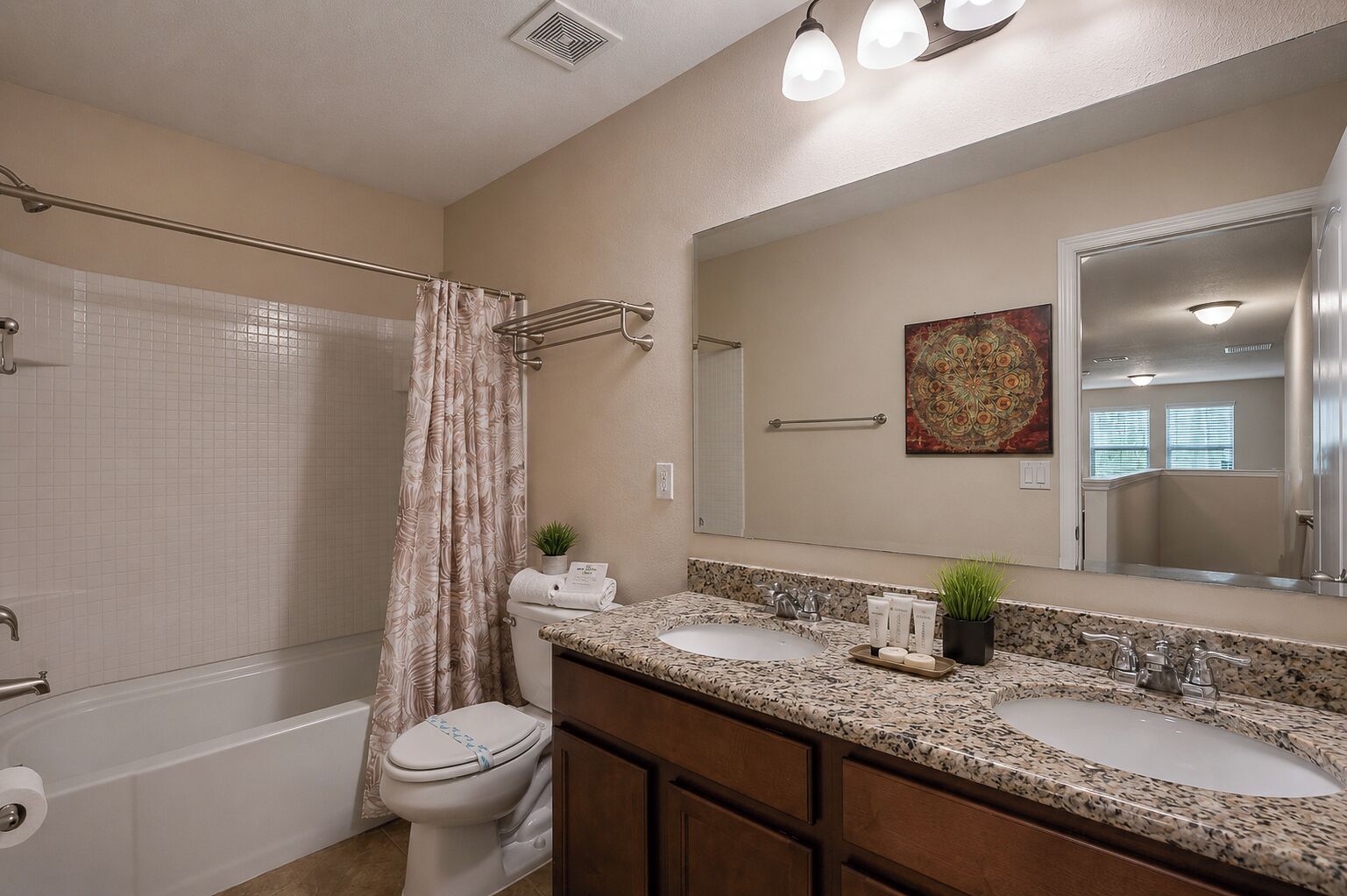 A bathroom with a shower, toilet, two sinks, a large mirror, and a decorative plant.