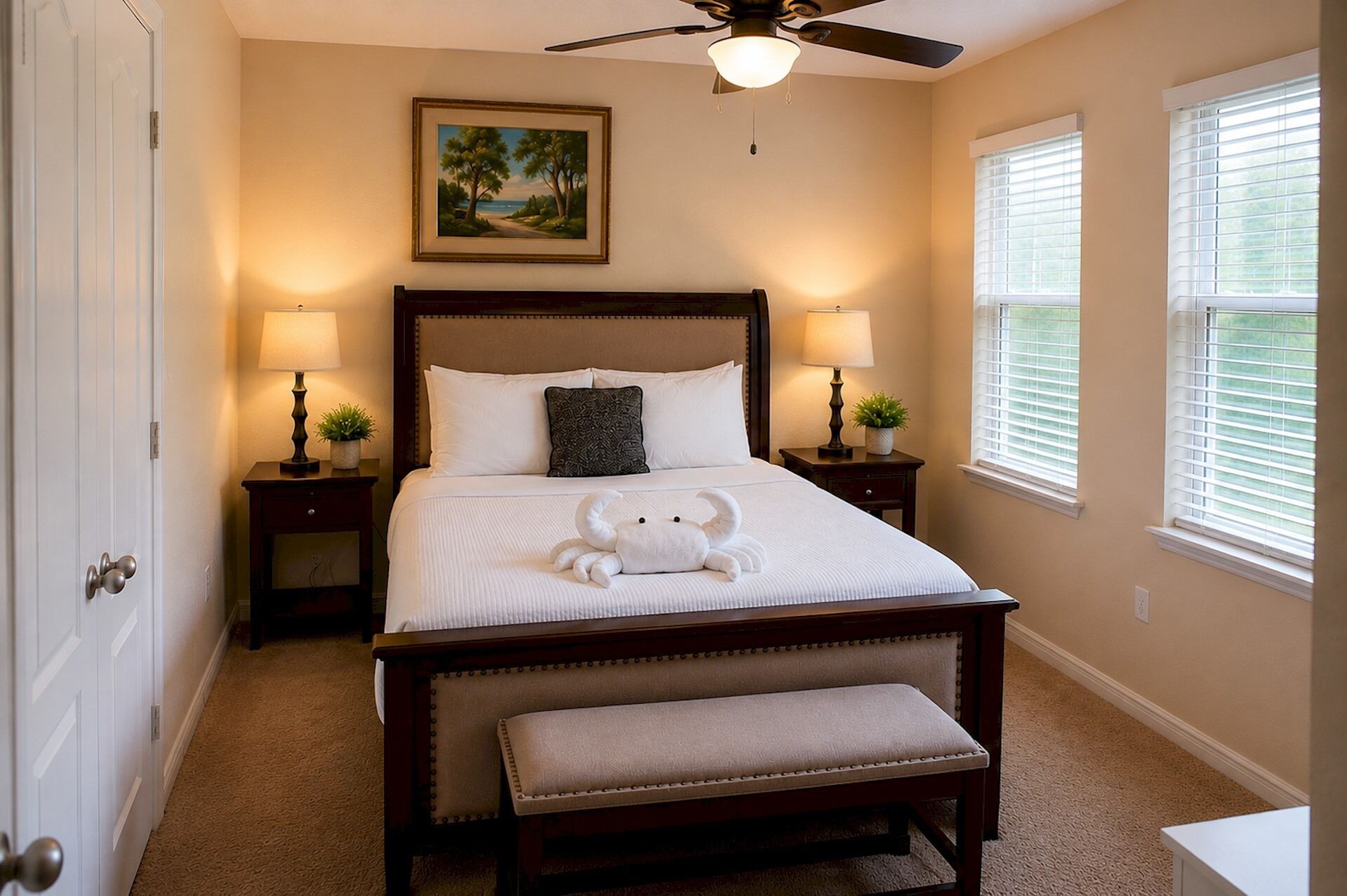 A bedroom with a bed, bedside lamps, a ceiling fan, a painting, and windows.