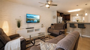 Ein modernes Wohnzimmer mit Flachbildfernseher, Deckenventilator, Glastisch und Sofa.