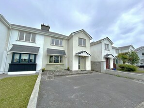 A residential street with houses, a paved driveway, and a grassy area.