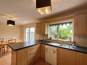 Una cocina con armarios de madera, lavavajillas, pileta y ventana con vista a follaje.