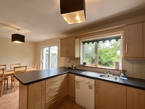 A kitchen with a dishwasher, a window with a view of greenery, and a dining area with chairs.