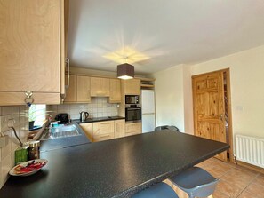 A compact kitchen with a black countertop, wooden cabinets, a microwave, and a refrigerator. - An Tulan Cleasach Spiddal (Spiddal)
