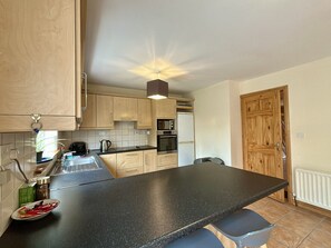 A kitchen with wooden cabinets, a black countertop, a refrigerator, and a wooden door.