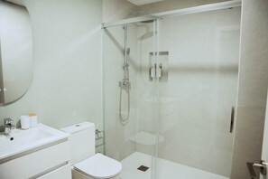 A modern bathroom with a glass-enclosed shower, a white sink, and a toilet. - Olea Suites Conil · 1 (Conil de la Frontera)