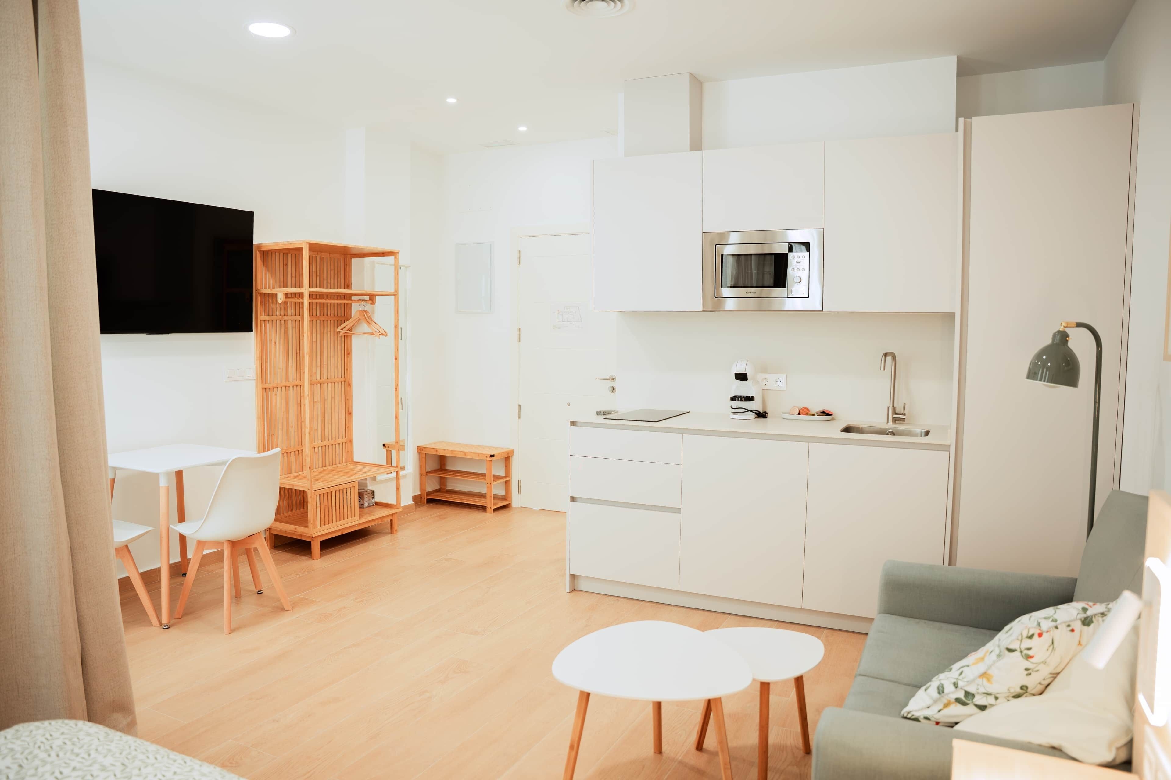 Una habitación moderna y luminosa, con kitchenette, comedor con mesa y sillas, y zona de estar con sofá.