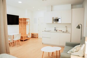 Ein moderner, gut beleuchteter Raum mit Küchenzeile, einem Essbereich mit Tisch und Stühlen sowie einer Sitzecke mit einer Couch.