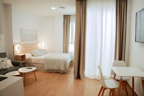 Ein modernes Hotelzimmer mit Bett, einer Couch, einem Esstisch und einem Sessel.