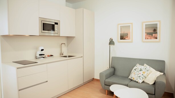 Ein kompakter Wohnbereich mit Küchenzeile, einer Couch, einem kleinen Tisch und zwei gerahmten Bildern an der Wand.