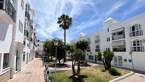 A residential area with white buildings, a paved walkway, and a palm tree. - Olea Suites Conil · 4 (Conil de la Frontera)