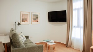 A modern living room with a sofa, a small table, a TV, and two framed pictures on the wall. - Olea Suites Conil · 4 (Conil de la Frontera)