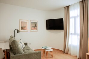 Ein modernes Wohnzimmer mit einer Couch, einem kleinen Tisch, einem Fernseher und zwei gerahmten Bildern an der Wand.