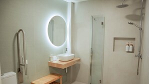 A modern bathroom with a glass-enclosed shower, a wooden vanity, a round mirror, and a toilet. - Olea Suites Conil · 4 (Conil de la Frontera)
