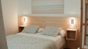 A neatly arranged bedroom with a bed, two bedside tables, and a wall-mounted light fixture. - Olea Suites Conil · 5 (Conil de la Frontera)