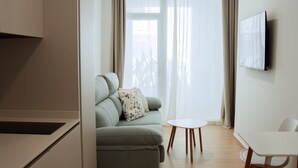 A modern living room with a sofa, a small round table, and a TV mounted on the wall. - Olea Suites Conil · 5 (Conil de la Frontera)