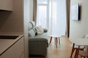 A modern living room with a sofa, a small round table, and a TV mounted on the wall. - Olea Suites Conil · 5 (Conil de la Frontera)