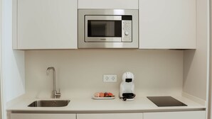 A compact kitchenette with a stainless steel microwave, a coffee maker, a sink, and a small plate with food items. - Olea Suites Conil · 5 (Conil de la Frontera)