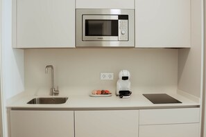 A compact kitchenette with a stainless steel microwave, a coffee maker, a sink, and a small plate with food items. - Olea Suites Conil · 5 (Conil de la Frontera)
