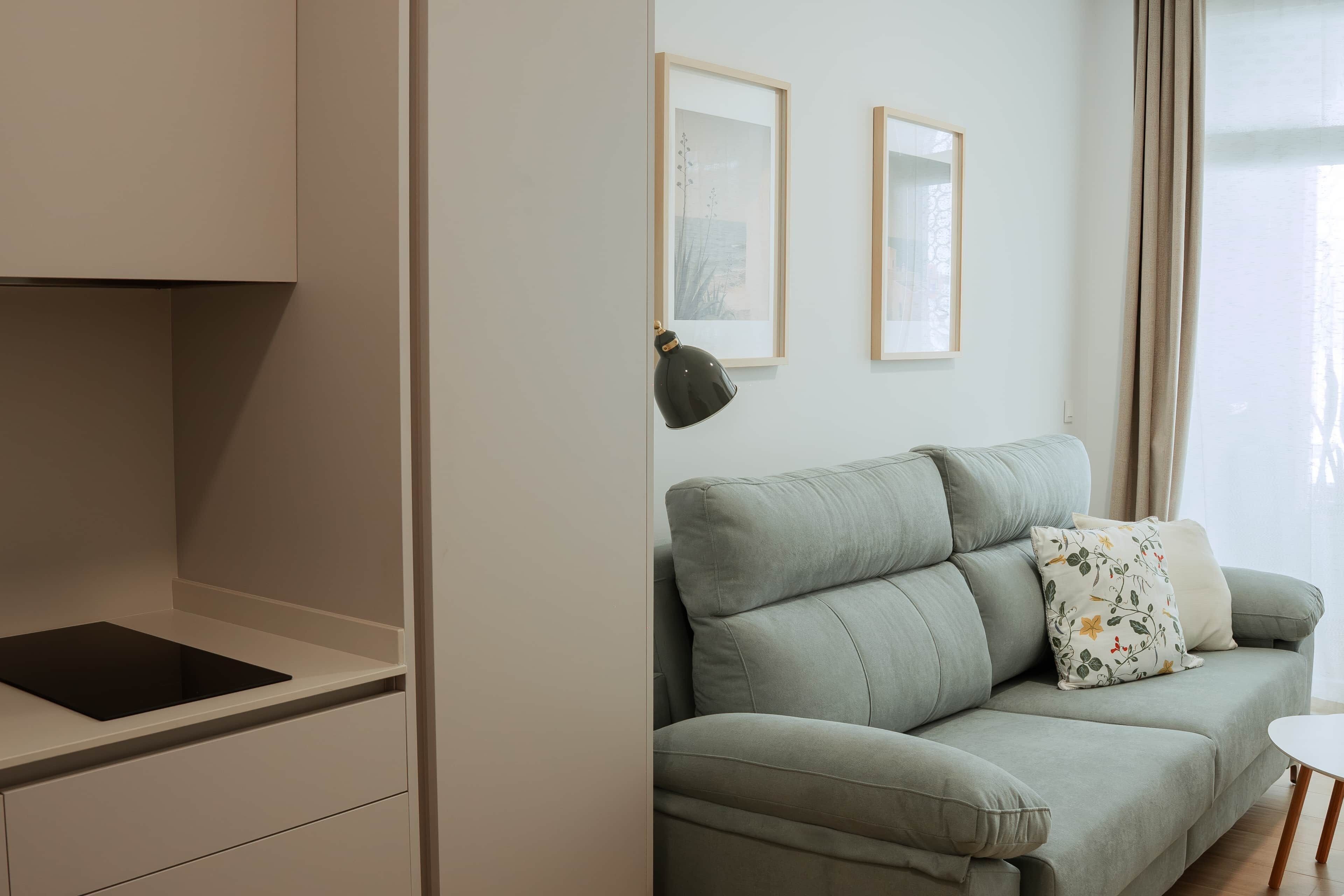 A modern living room with a sofa, a side table, and a kitchen area with a countertop and cabinets.