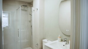 A modern bathroom with a glass-enclosed shower, a white sink, and a large mirror. - Olea Suites Conil · 5 (Conil de la Frontera)