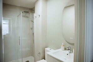 A modern bathroom with a glass-enclosed shower, a white sink, and a large mirror. - Olea Suites Conil · 5 (Conil de la Frontera)