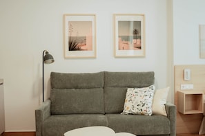 Ein graues Sofa mit einem floralen Kissen, eine schwarze Stehlampe und zwei gerahmte Bilder an der Wand.