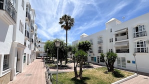 A residential area with white buildings, a paved walkway, and a palm tree. - Olea Suites Conil · 2 (Conil de la Frontera)