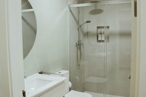 Ein modernes Badezimmer mit einer gläsernen Duschkabine, einem weißen Waschbecken und einer Toilette.