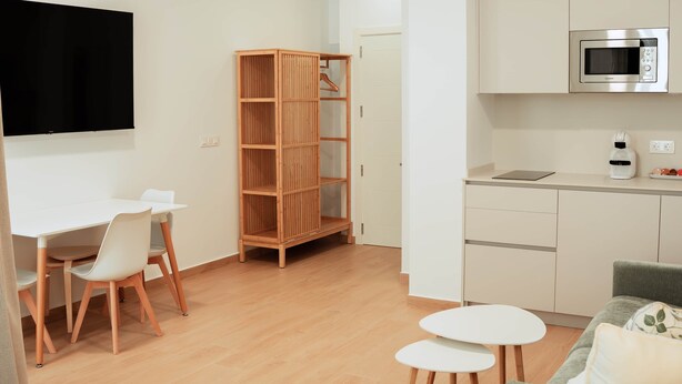 A modern kitchen with a microwave, a wooden cabinet, and a dining area with a table and chairs. - Olea Suites Conil · 2 (Conil de la Frontera)