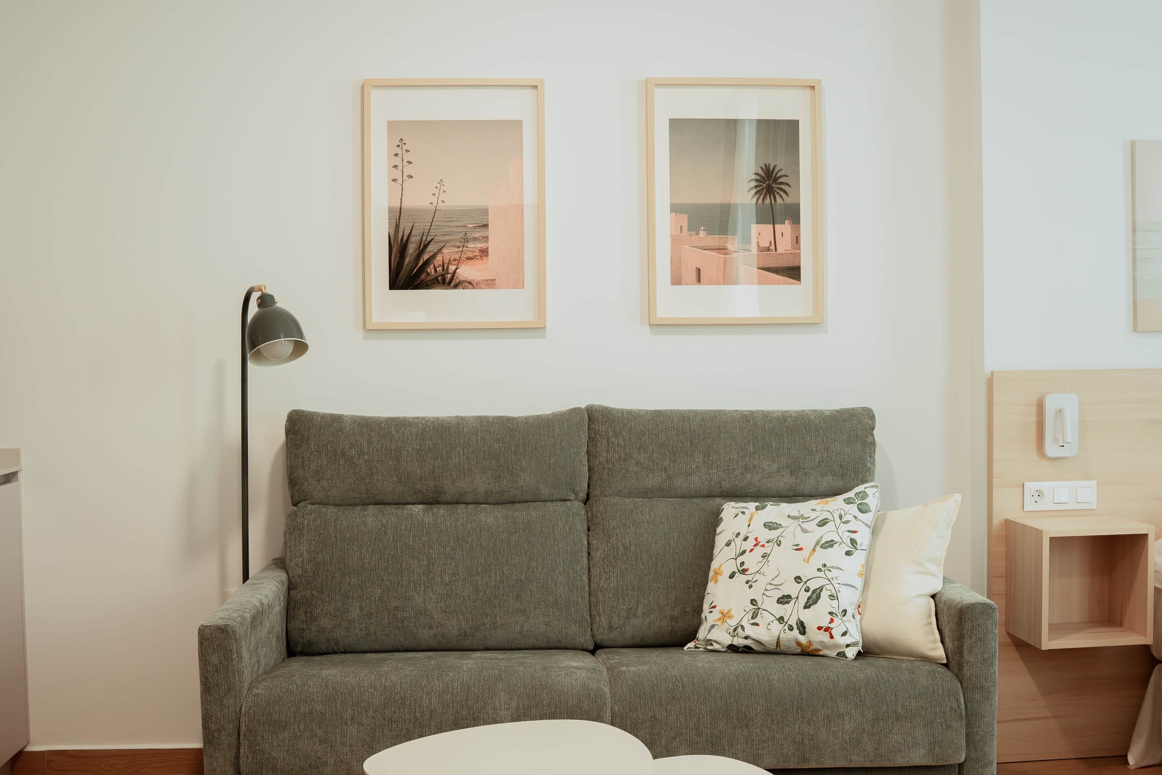 A grey sofa with a floral pillow, a black floor lamp, and two framed pictures on the wall.